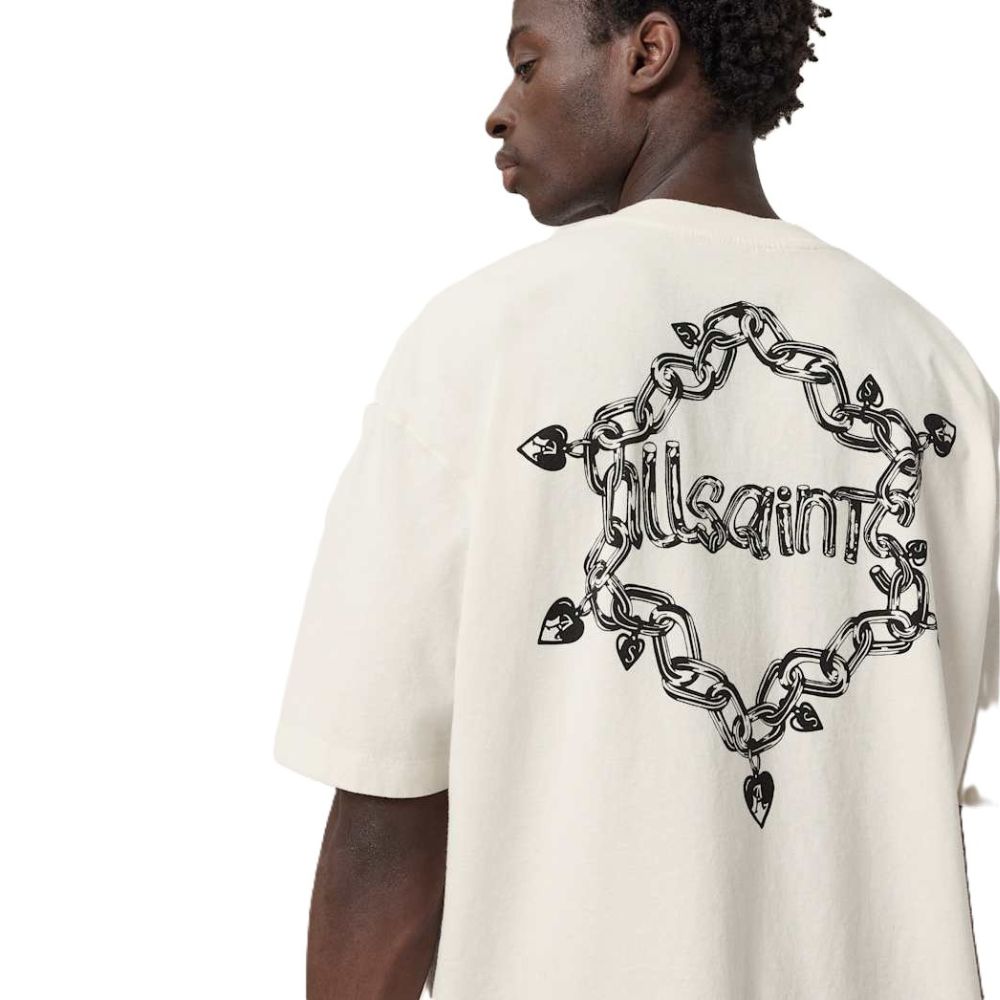 A man shown from the back wearing an oversized off-white t-shirt with a large black graphic on the back. The graphic features a heart-shaped chain design with the word 'Allsaints' in stylized script inside.