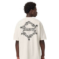 A man shown from the back wearing a cream-colored oversized t-shirt with a large black graphic on the back. The graphic features a chain-link heart design with the word 'Kith' in the center.
