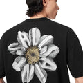 A person shown from the back wearing a black short-sleeve T-shirt with a large grayscale flower graphic on the back, featuring a yellow-brown center.