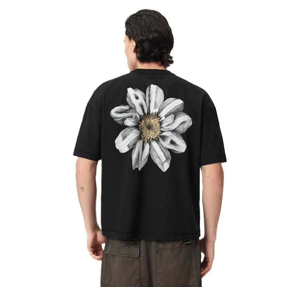 A man viewed from behind wearing a black t-shirt with a large white and gray daisy graphic on the back, paired with brown cargo pants, against a plain white background.