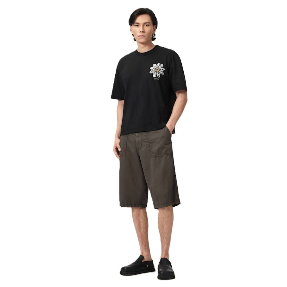 A man modeling a black short-sleeve t-shirt with a white graphic print on the left chest, paired with dark olive brown shorts and black slip-on shoes, against a plain white background.