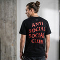A man wearing a black t-shirt with 'ANTI SOCIAL SOCIAL CLUB' printed in red across the back, shown from behind in an indoor setting.