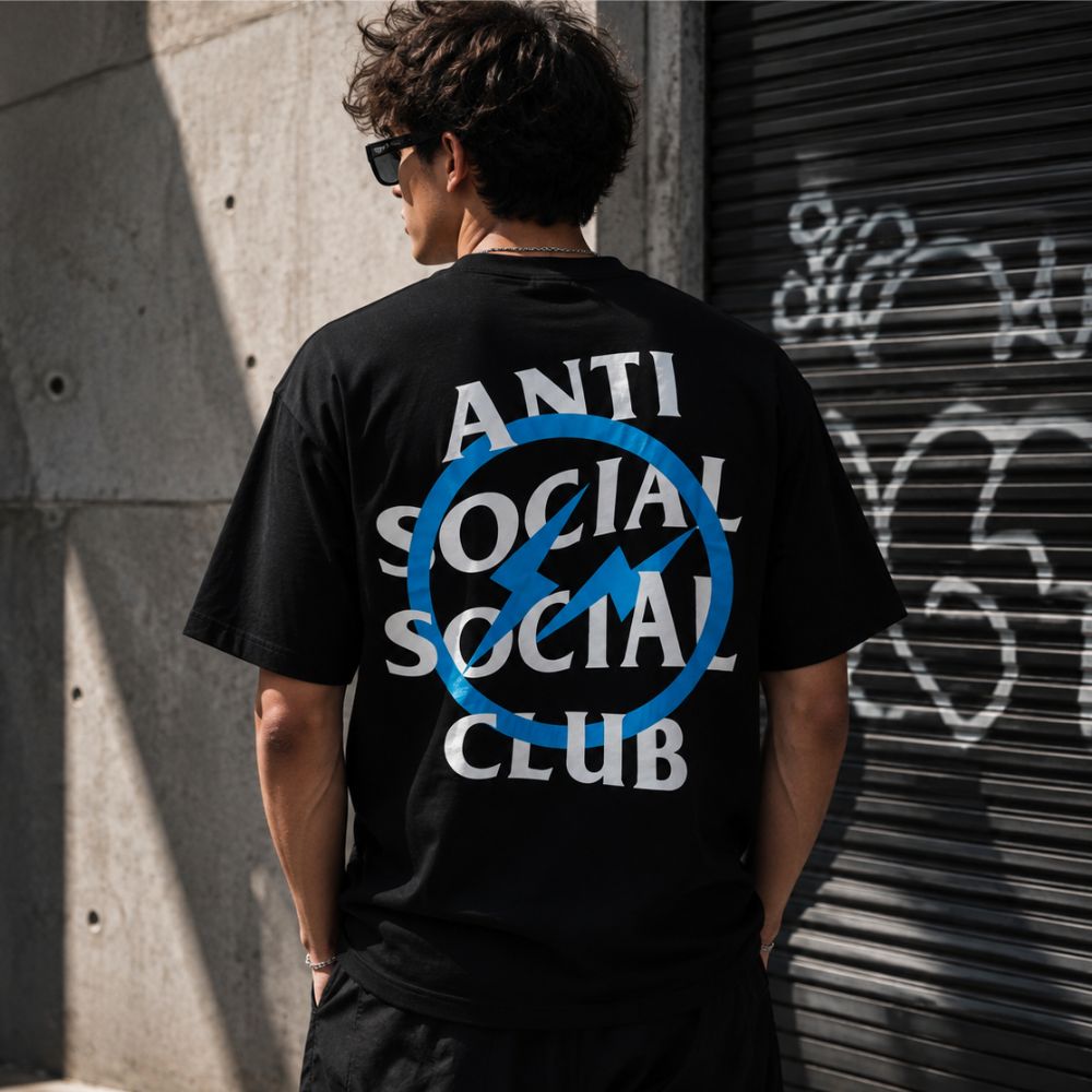 A man viewed from behind wearing a black t-shirt with a large graphic on the back. The graphic features the text 'ANTI SOCIAL SOCIAL CLUB' in white, overlaid with a blue circle and slash symbol.