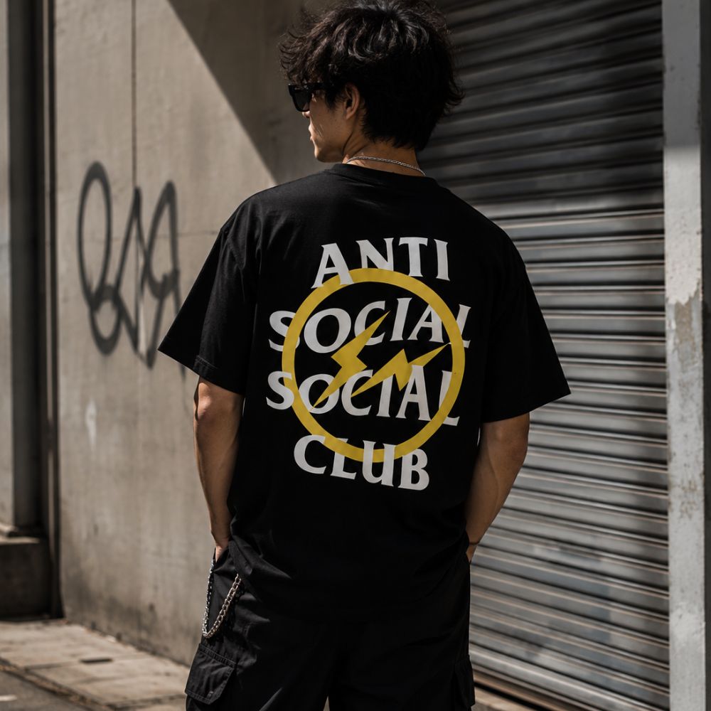 A black short-sleeve t-shirt with a yellow and white circular graphic on the left chest reading 'ANTI SOCIAL CLUB'.