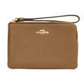 A Coach pebbled leather wristlet pouch in tan brown, featuring a top zipper with gold-tone hardware, a wrist strap, and the gold Coach logo on the front.