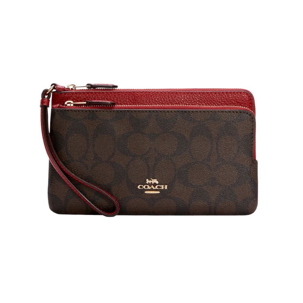 A Coach wristlet clutch in dark brown signature monogram canvas with a red pebbled leather top trim and wrist strap, featuring a gold-tone Coach logo on the front.