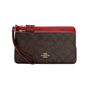 A Coach wristlet clutch in dark brown signature monogram canvas with a red pebbled leather top trim and wrist strap, featuring a gold-tone Coach logo on the front.