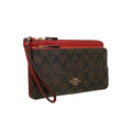 A Coach wristlet clutch in the signature brown monogram canvas with a vibrant red leather trim and wrist strap, featuring gold-tone hardware and a visible Coach logo on the front.