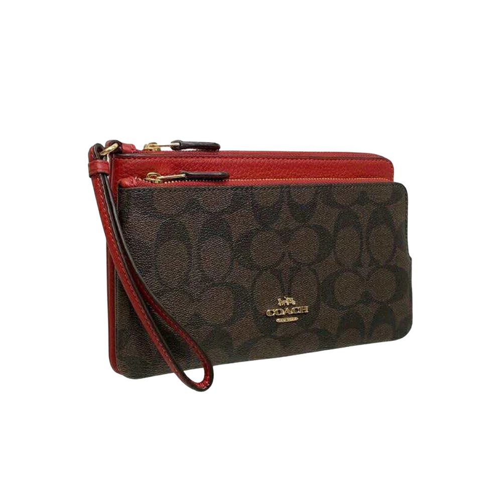 A Coach wristlet clutch in the signature brown monogram canvas with a vibrant red leather trim and wrist strap, featuring gold-tone hardware and a visible Coach logo on the front.
