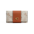 A Coach wallet in the brand's signature monogram canvas, featuring a vertical tan leather band with a gold-tone 'C' logo clasp, set against a plain white background.