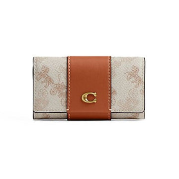 A Coach wallet in the brand's signature monogram canvas, featuring a vertical tan leather band with a gold-tone 'C' logo clasp, set against a plain white background.