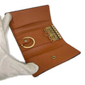 A tan leather key ring case with gold-tone hardware, held open by a white gloved hand against a white background.