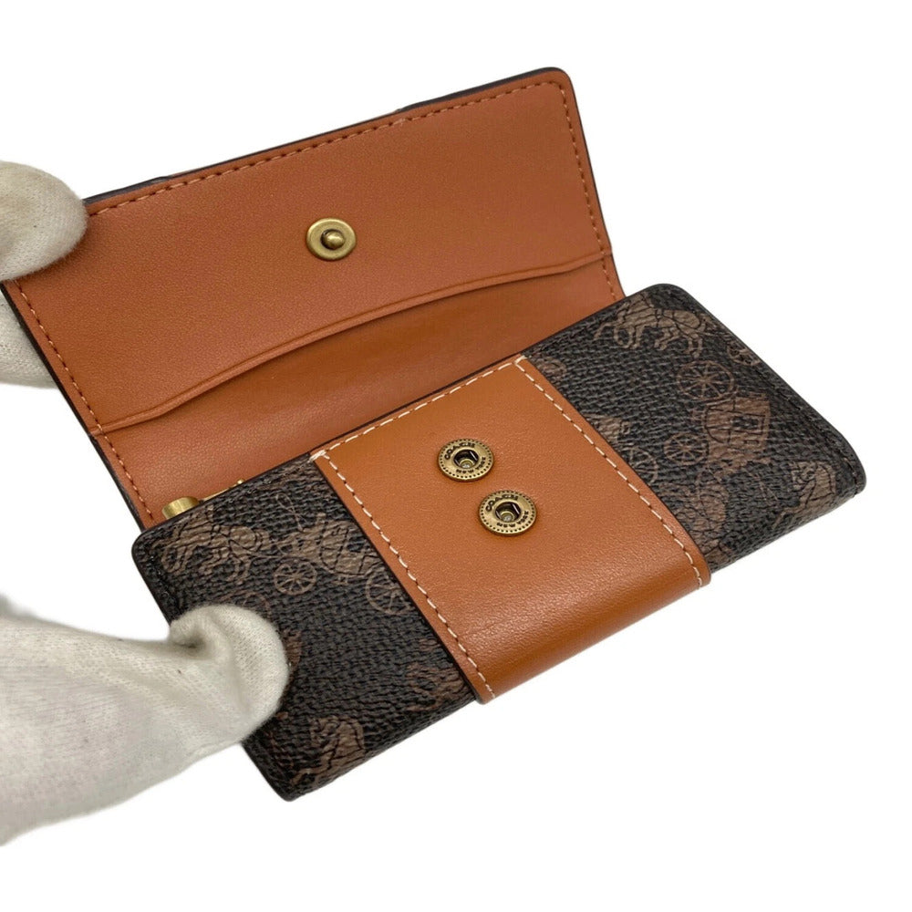 A Louis Vuitton monogram canvas and tan leather wallet held open by a white gloved hand, showing its interior card slots and snap-button closure on a white background.