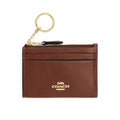 A brown leather card holder keychain with gold-tone hardware and the Coach logo on the front, shown against a plain white background.