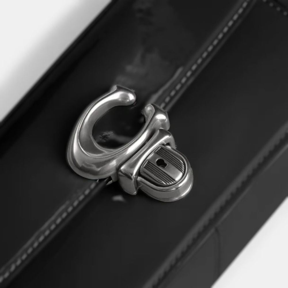 Close-up of a black leather strap with a polished silver metal clasp on a black bag, photographed against a white background.