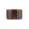 A Coach card holder wallet featuring the brand's signature monogram canvas in brown and beige, with a solid dark brown leather center panel and a gold-tone 'C' logo on the front.