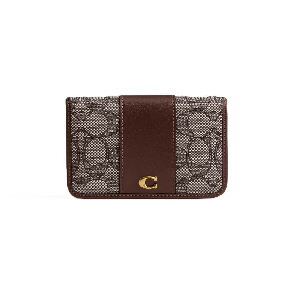 A Coach card holder wallet featuring the brand's signature monogram canvas in brown and beige, with a solid dark brown leather center panel and a gold-tone 'C' logo on the front.