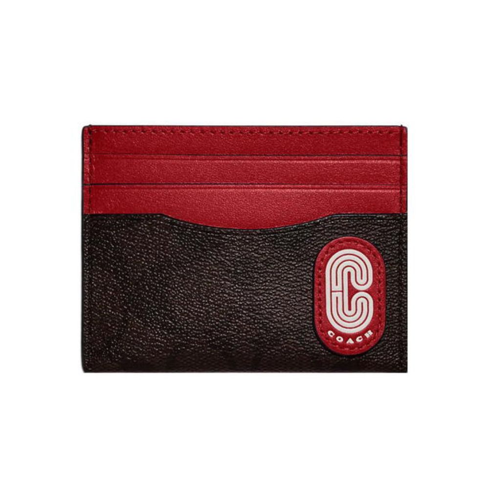 A Coach card holder wallet in textured dark brown and red leather, featuring a red leather top band and a red oval patch with a white embroidered 'C' logo and 'COACH' text.