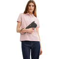 Woman wearing a pink polo shirt and dark jeans, holding a black leather wallet.