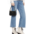 A model wearing light-wash blue cropped flare jeans, white lace-up ankle boots, and holding a black quilted shoulder bag with gold hardware against a white background.