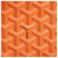 Orange Goyard canvas fabric with the brand's signature repeating chevron pattern in white and dark brown, featuring a central handwritten signature.