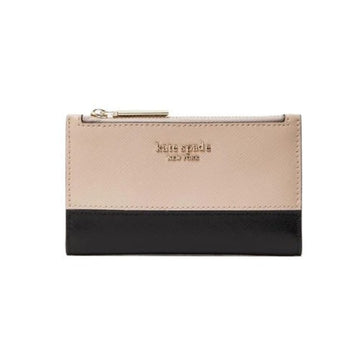 A Kate Spade New York zip-around wallet in a two-tone color-blocked design, featuring a light beige textured leather top half and a black leather bottom half, with gold-tone hardware and logo lettering.