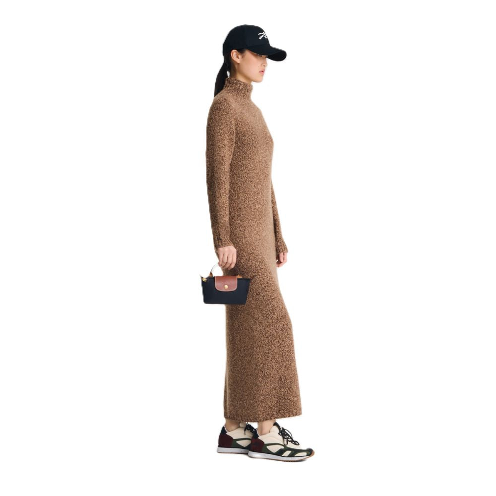 A woman in profile wearing a brown textured knit turtleneck maxi dress, a black baseball cap, and sneakers, holding a small black handbag against a plain white background.