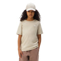 A child model wearing a light beige short-sleeve crewneck t-shirt with a small white chest logo, a matching beige baseball cap, and dusty rose pants, photographed against a solid white background.