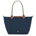 A navy blue nylon tote bag with brown leather handles and a matching brown leather top handlebar, featuring a small gold snap button on the front.