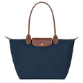 Navy blue tote bag with brown leather handle and trim on a white background