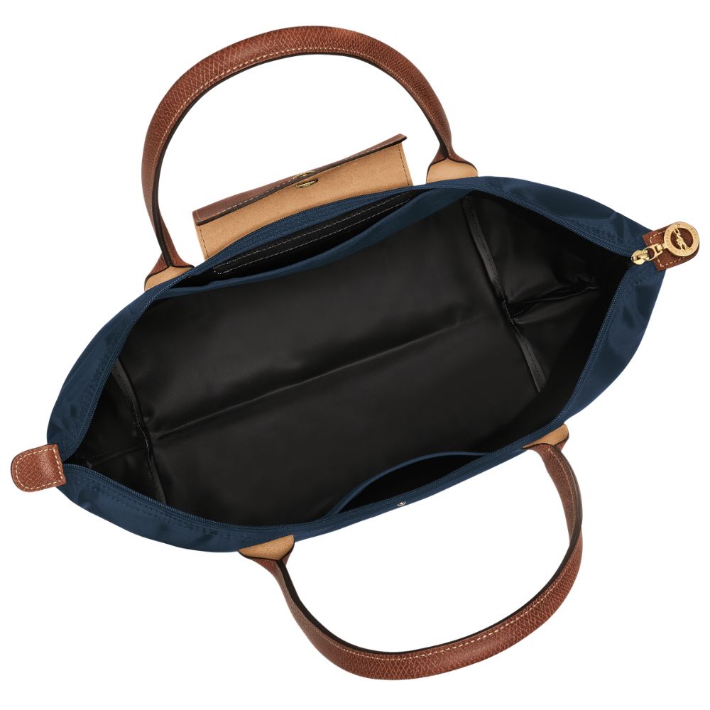 An overhead view of an open navy blue handbag with brown leather handles, a black interior lining, and gold-tone hardware on a white background.