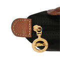 Close-up of a black nylon bag with brown leather trim and a gold-tone zipper pull featuring the Longchamp horse logo and 'LONGCHAMP 1946' text.