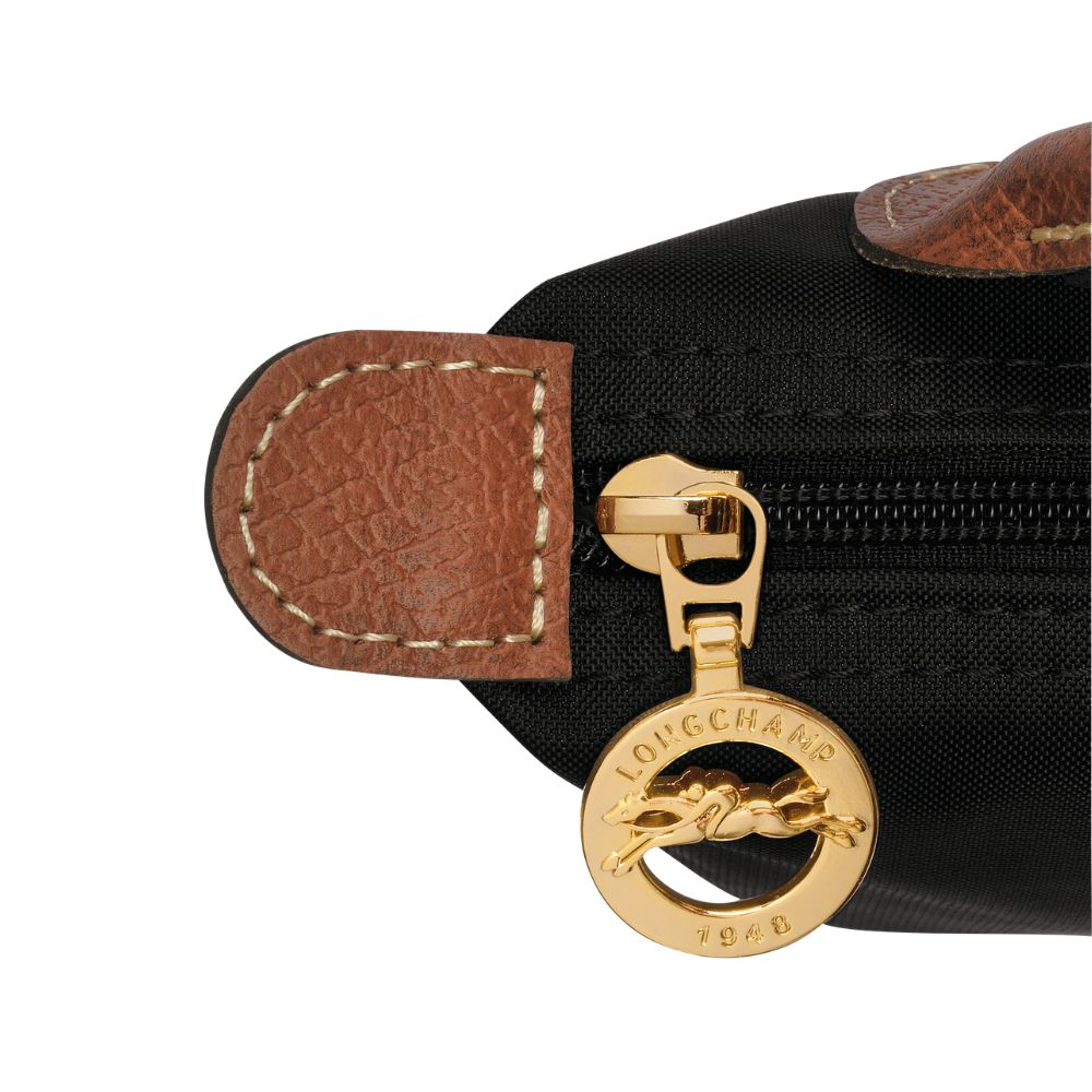 Close-up of a black nylon bag with brown leather trim and a gold-tone zipper pull featuring the Longchamp horse logo and 'LONGCHAMP 1946' text.