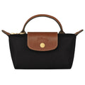 A black nylon handbag with a brown leather top handle, zipper trim, and front flap featuring a gold-tone circular logo button.
