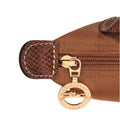 Close-up of a brown textured leather and canvas zippered pouch with a gold-tone Longchamp horse logo zipper pull on a white background.
