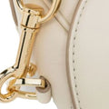 Close-up of a cream-colored leather handbag with polished gold-tone hardware, showing a stitched leather edge and a gold horsebit-style clasp.