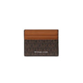 Michael Kors card holder in brown monogram canvas with a lighter brown leather stripe across the top, featuring the MICHAEL KORS logo in white on the front, set against a plain white background.