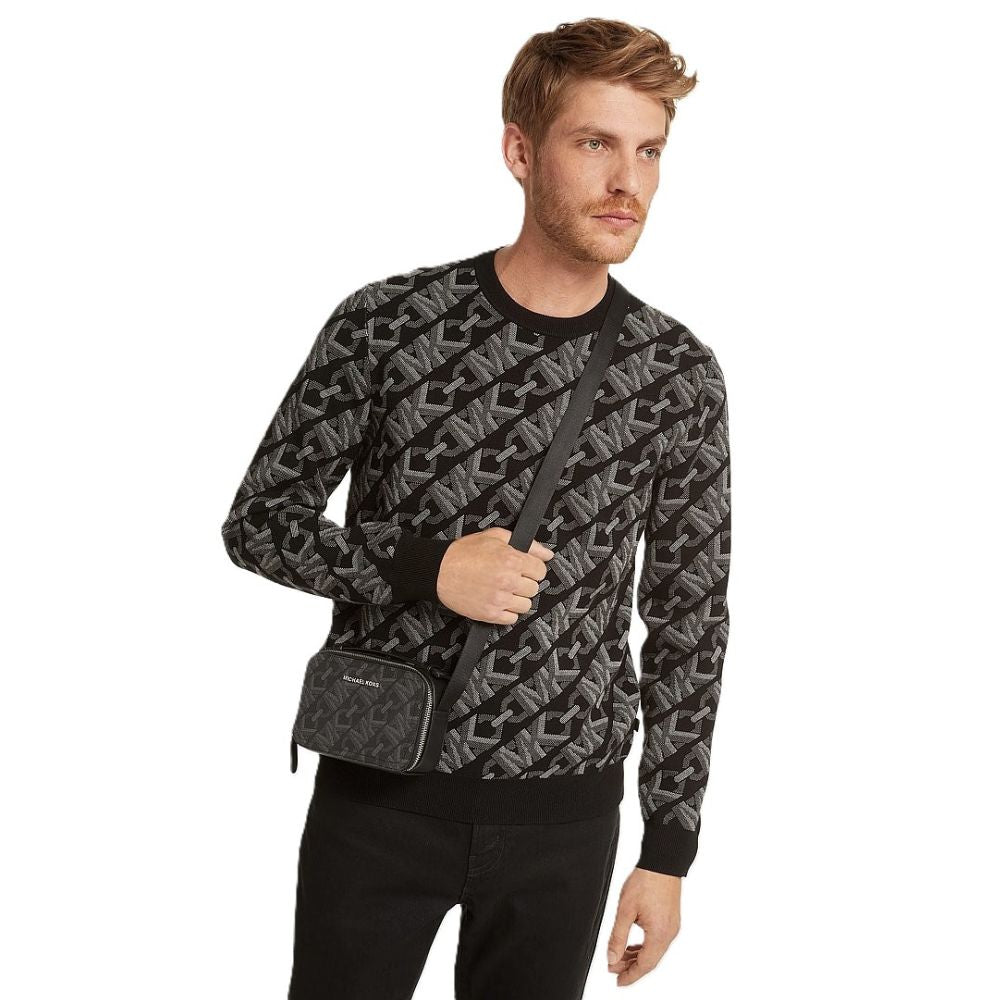 A man wearing a black and gray monogram pattern crewneck sweatshirt and black pants, carrying a black crossbody bag with a matching monogram pattern.