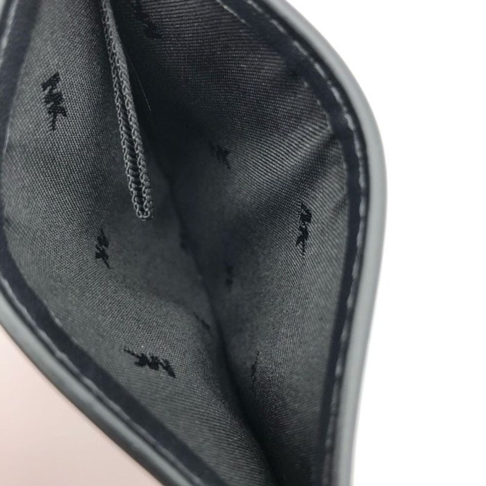 Close-up of the interior lining of a dark gray or black pouch or wallet, showing a woven fabric surface with a subtle repeating black motif and stitched edge.