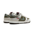 A pair of Nike Dunk Low sneakers in olive green, off-white, and light gray, featuring a red embroidered 'TIMELAPSE' logo on the side and a dark gray outsole.
