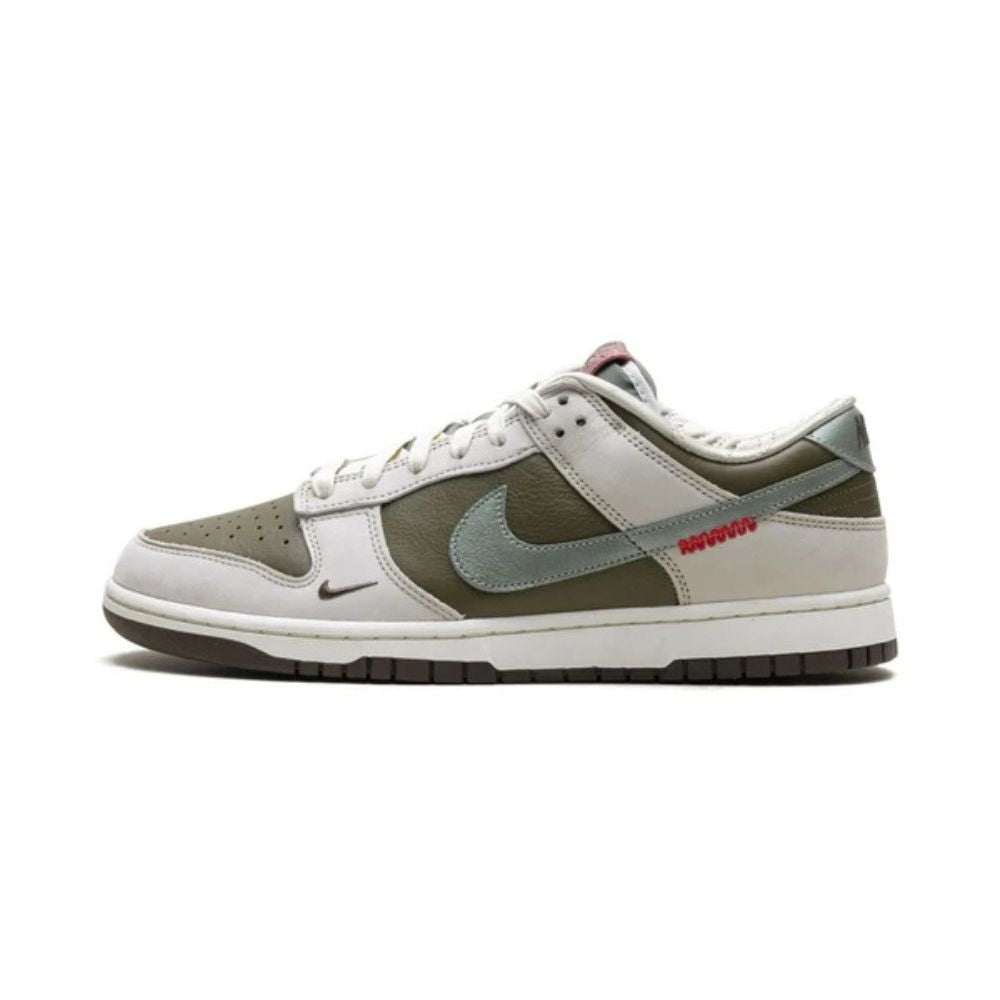 A Nike Dunk sneaker in a muted colorway featuring olive green, light gray, and white panels, with a small red 'SOURDAN' text detail on the side.