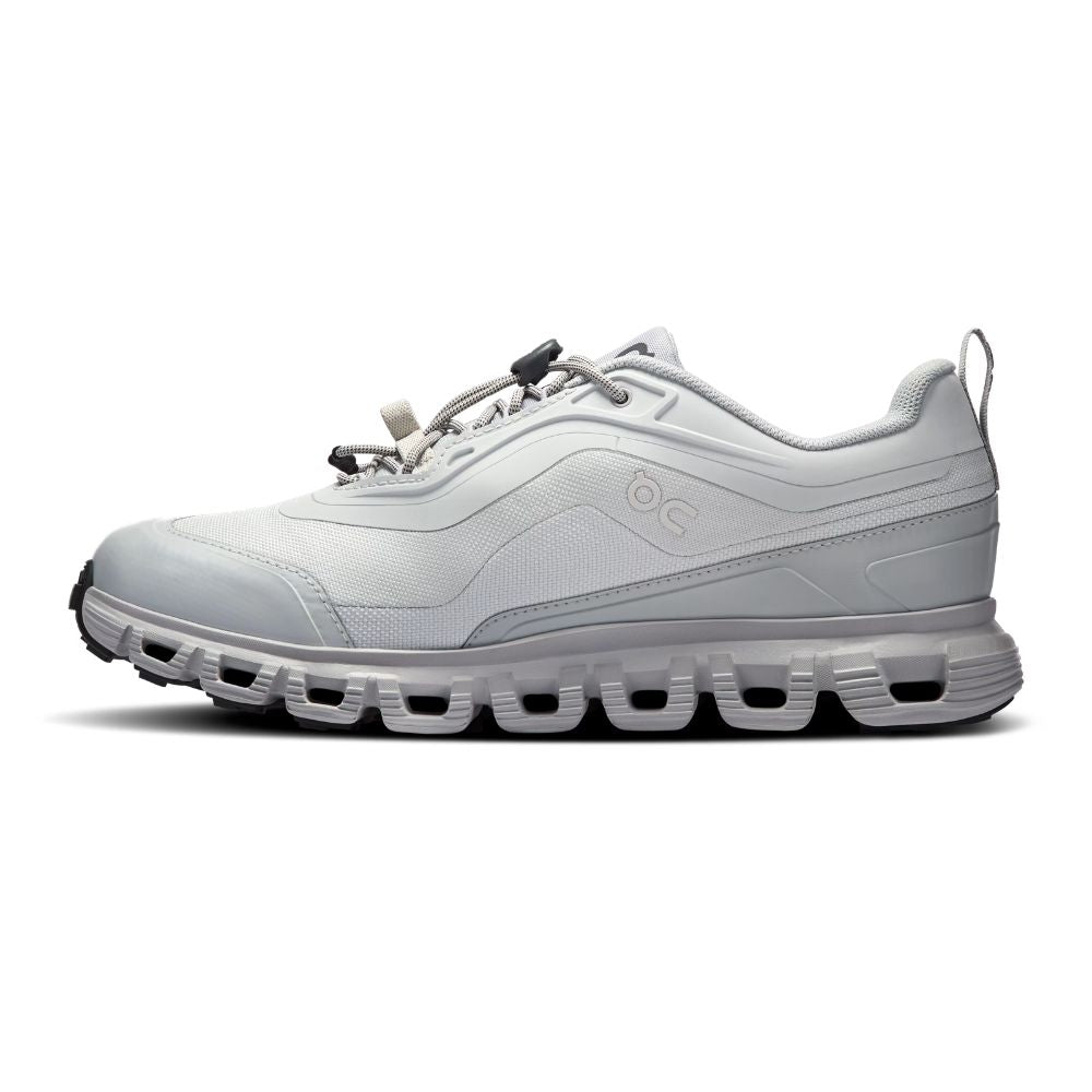 A light gray and white low-top athletic sneaker shown from the side profile on a clean white background. The shoe features a textured mesh upper, a chunky sculpted sole with circular cutouts, and a small embossed logo on the side.