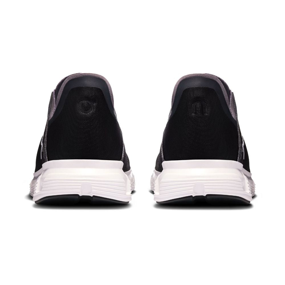 A pair of black slip-on sneakers shown from the back, featuring a thick white midsole and a small circular logo on the heel counter, set against a plain white background.