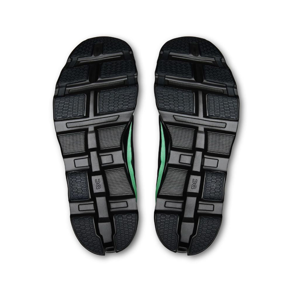 A pair of athletic shoes shown from the sole view, displaying black textured rubber outsoles with a vibrant green accent stripe running vertically along the center.