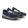 A pair of On running shoes in navy blue and light gray, featuring a breathable mesh upper, light beige laces, and a distinctive cushioned sole, shown on a white background.