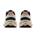 A pair of athletic sneakers shown from the rear, featuring a cream-colored chunky sole, a white and black upper, and a textured orange-to-black gradient heel tab.