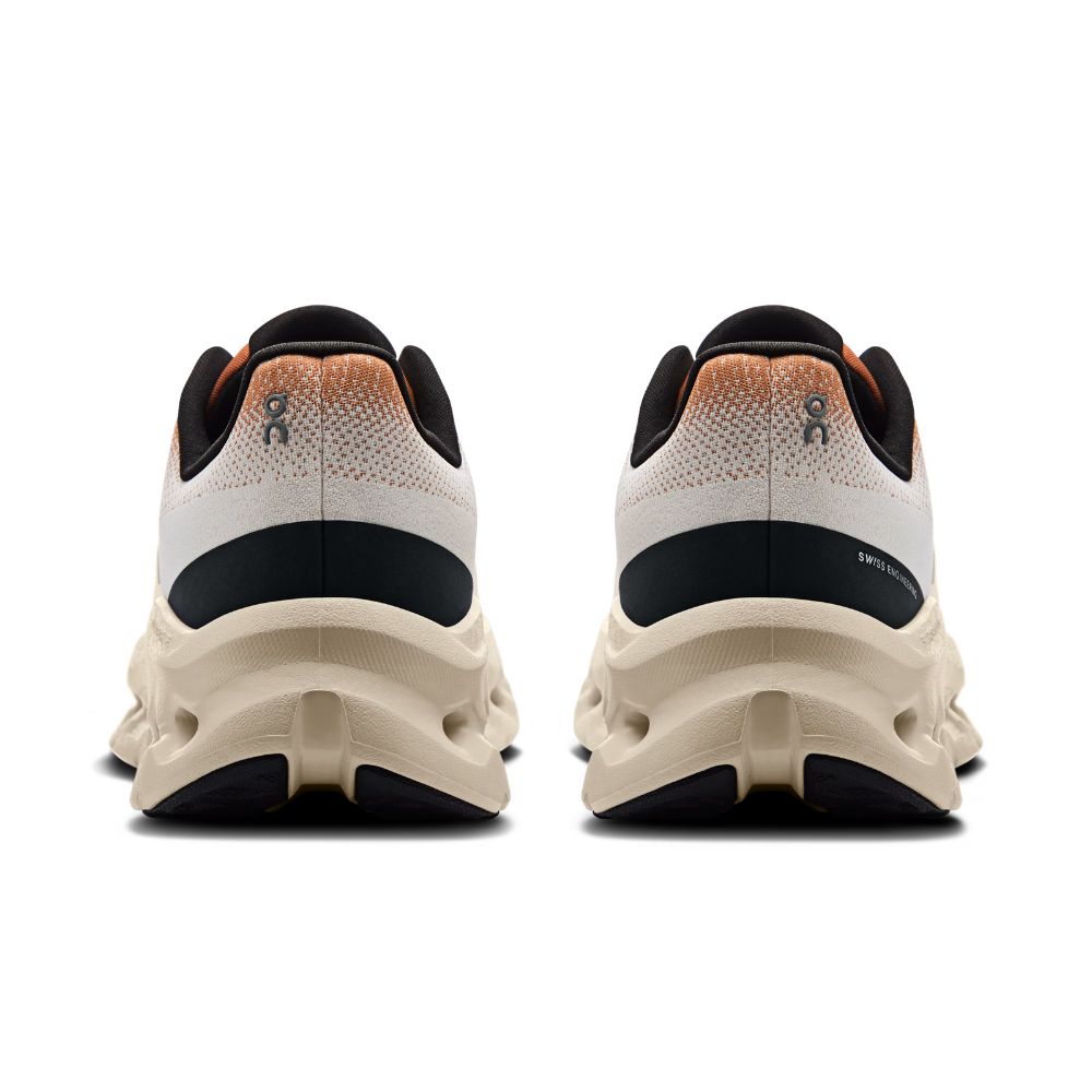 A pair of athletic sneakers shown from the rear, featuring a cream-colored chunky sole, a white and black upper, and a textured orange-to-black gradient heel tab.
