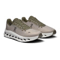A pair of On running shoes in a light taupe-beige and olive green colorway, featuring a chunky white cushioned sole with black cutouts, shown on a white background.