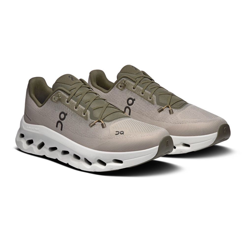 A pair of On running shoes in a light taupe-beige and olive green colorway, featuring a chunky white cushioned sole with black cutouts, shown on a white background.