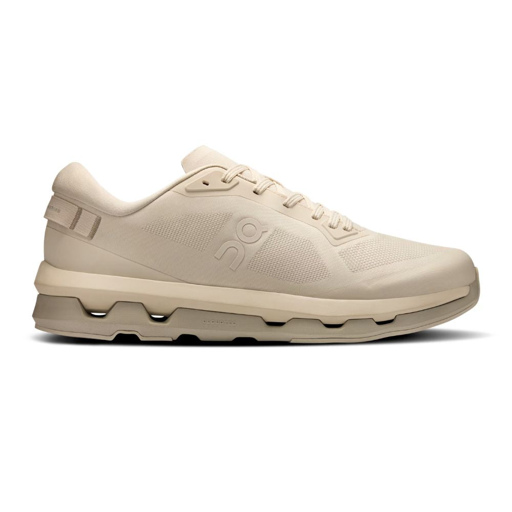 A single low-top sneaker in a uniform light beige/cream color, shown from the side against a plain white background. The shoe features a textured mesh upper, matching beige laces, a tonal embossed logo on the side, and a chunky wavy midsole.